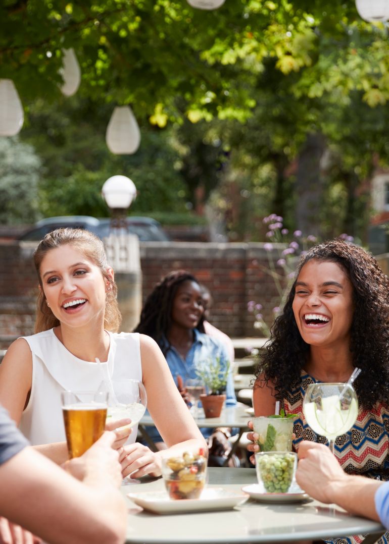 Friends sharing a laugh in a pub garden with refreshing summer drinks
